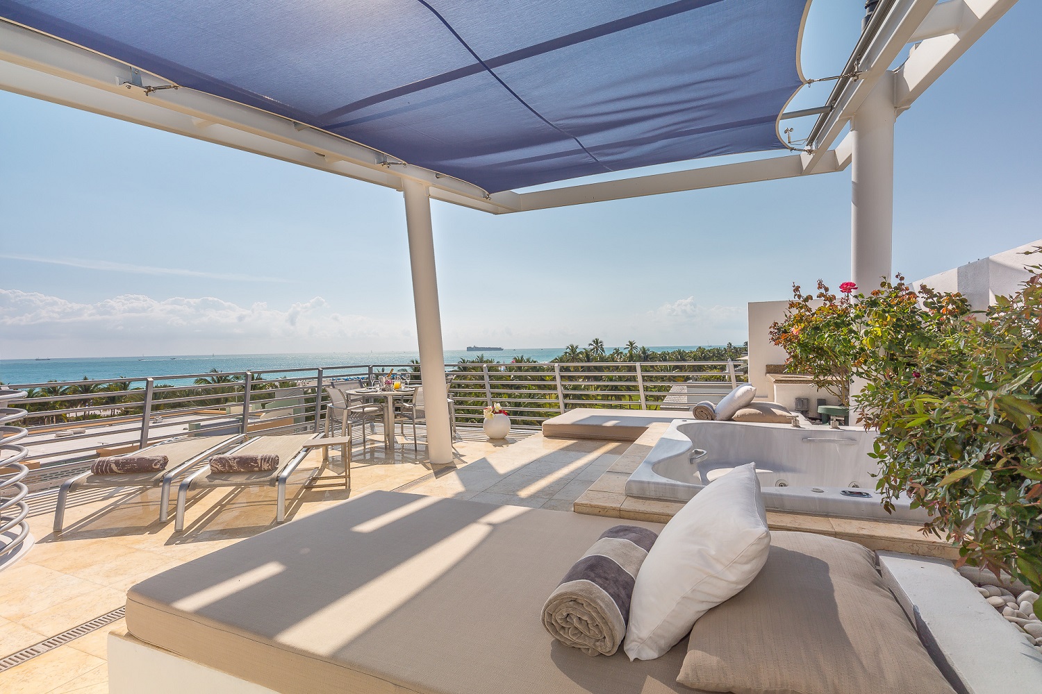 A daybed and pergola on a rooftop patio overlooking the ocean.